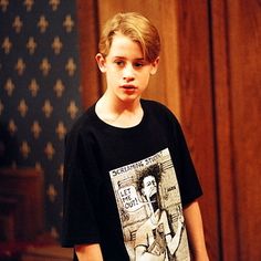 a young boy is standing in front of an american flag and wearing a t - shirt