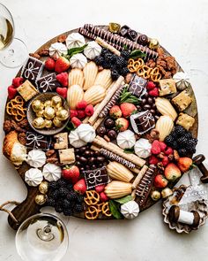 a platter filled with assorted snacks and desserts next to two glasses of wine