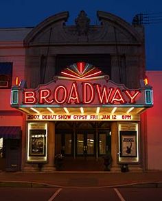 the broadway sign lit up at night in front of a building with its lights on