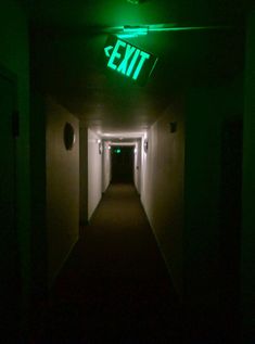 an exit sign is lit up in the dark with green light coming from behind it