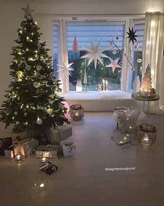 a christmas tree in front of a window with lit candles on the floor next to it