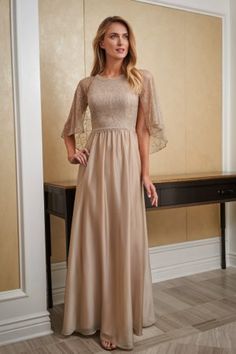 a woman standing in front of a desk wearing a long dress with sleeves on it