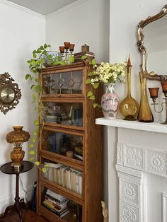 a book shelf filled with lots of books next to a mirror and vases on top of it