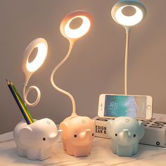 three elephant shaped lamps sitting on top of a table next to a cell phone and pencil holder