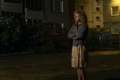 a woman standing in front of a building at night with her arms crossed and looking off to the side