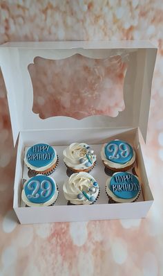 a box filled with cupcakes covered in frosting and blue icing on top of a table