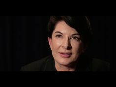 a woman with short hair wearing a black shirt and jacket looking at the camera while standing in front of a black background