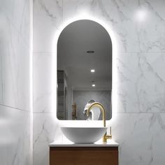 a bathroom with marble walls and white counter top, gold faucet sink and round mirror