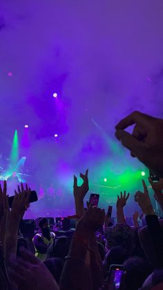 a crowd of people at a concert with their hands in the air and lights on