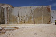 a man standing in front of a large wall with rocks and dirt on the ground