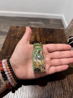 a person's hand holding a small bottle filled with gold and silver jewelry on top of a wooden table