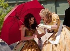 two women dressed in period clothing and holding red umbrellas while standing next to each other