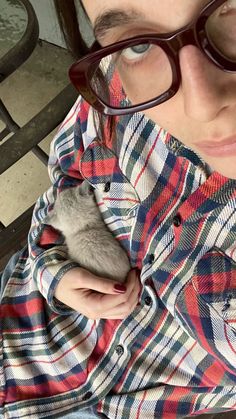 a woman holding a small mouse in her hands while wearing glasses and a plaid shirt