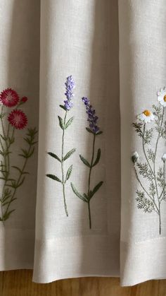 three different types of embroidered flowers on white linens hanging from a wooden table top