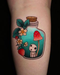 a small jar with mushrooms and flowers in it on the leg, next to a strawberry