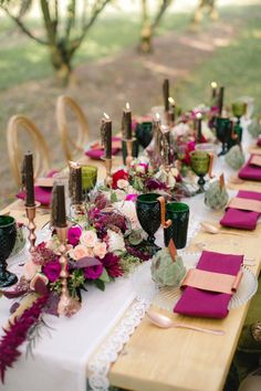 a long table with purple and green place settings on it, surrounded by greenery