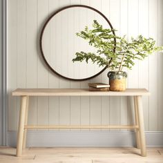 a wooden table with a potted plant on it and a round mirror above it