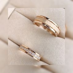 two gold wedding bands sitting on top of a white cloth covered surface with diamonds in the middle