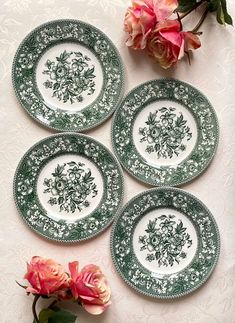 four green and white plates sitting on top of a table next to pink rose flowers