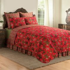 a bed with red and green comforters in a room next to a dresser, mirror and window