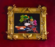 an ornate gold frame with fruit and vegetables in it on a red velvet wall background