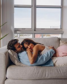 a man and woman cuddle on a couch in front of a window with the sun shining through