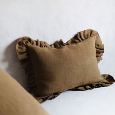 a brown pillow with ruffled edges on a white bedding set in front of a wall