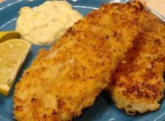 two pieces of fish on a blue plate with lemon wedges and mayonnaise