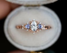 an engagement ring with three blue and white stones in it's center, sitting on top of a velvet box