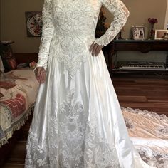 a woman in a white wedding dress standing next to a bed and looking at the camera