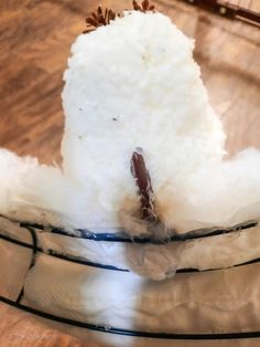 a snowman sitting on top of a wooden table next to a glass bowl filled with cotton