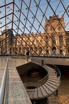 the inside of a glass building with stairs and people walking around in front of it