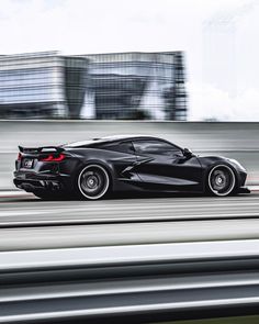 the black sports car is driving down the road in front of some buildings and skyscrapers