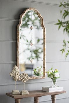 a wooden table topped with a mirror next to a vase filled with flowers and greenery