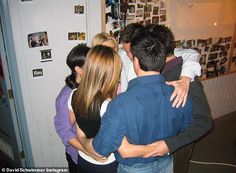 a group of people hugging each other in front of a wall with pictures on it