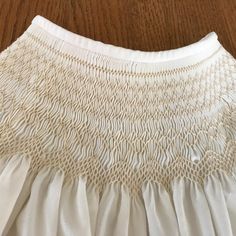 the back of a white dress on a wooden floor, with pleating and crochet