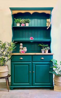 a green hutch with potted plants on the top and bottom shelf in front of it