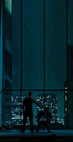 two people standing in front of large windows at night with city lights reflected on them