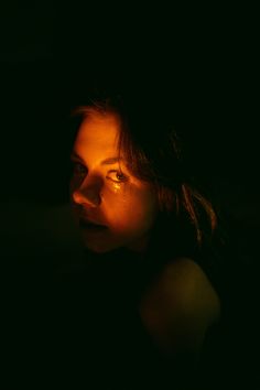 a woman in the dark with her eyes open and light shining down on her face