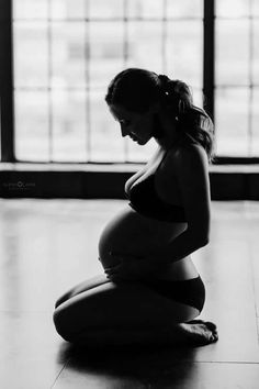 a pregnant woman sitting on the floor in front of a window with her belly exposed