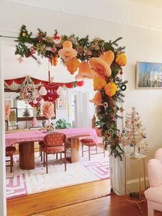 a dining room decorated for christmas with pink furniture and decorations on the walls, along with an arch made out of paper flowers