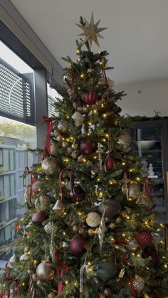 a christmas tree is decorated with red, gold and silver ornaments in front of a window