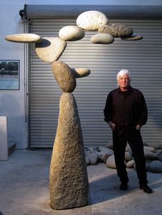 a man standing in front of a rock sculpture with rocks on top of it,