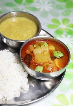 two metal bowls filled with food on top of a silver plate next to white rice