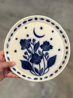 a hand is holding a blue and white plate with flowers on it, while the moon shines in the background