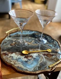 two martini glasses sitting on top of a marble tray next to a gold spoon and fork