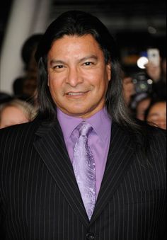 a man with long hair wearing a suit and purple shirt, smiling for the camera