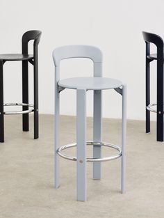 three stools in different colors and sizes on the floor with one chair up against the wall