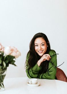 a woman sitting at a table with flowers in front of her and a vase on the table