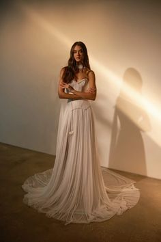 a woman standing in front of a white wall with her arms crossed and looking at the camera